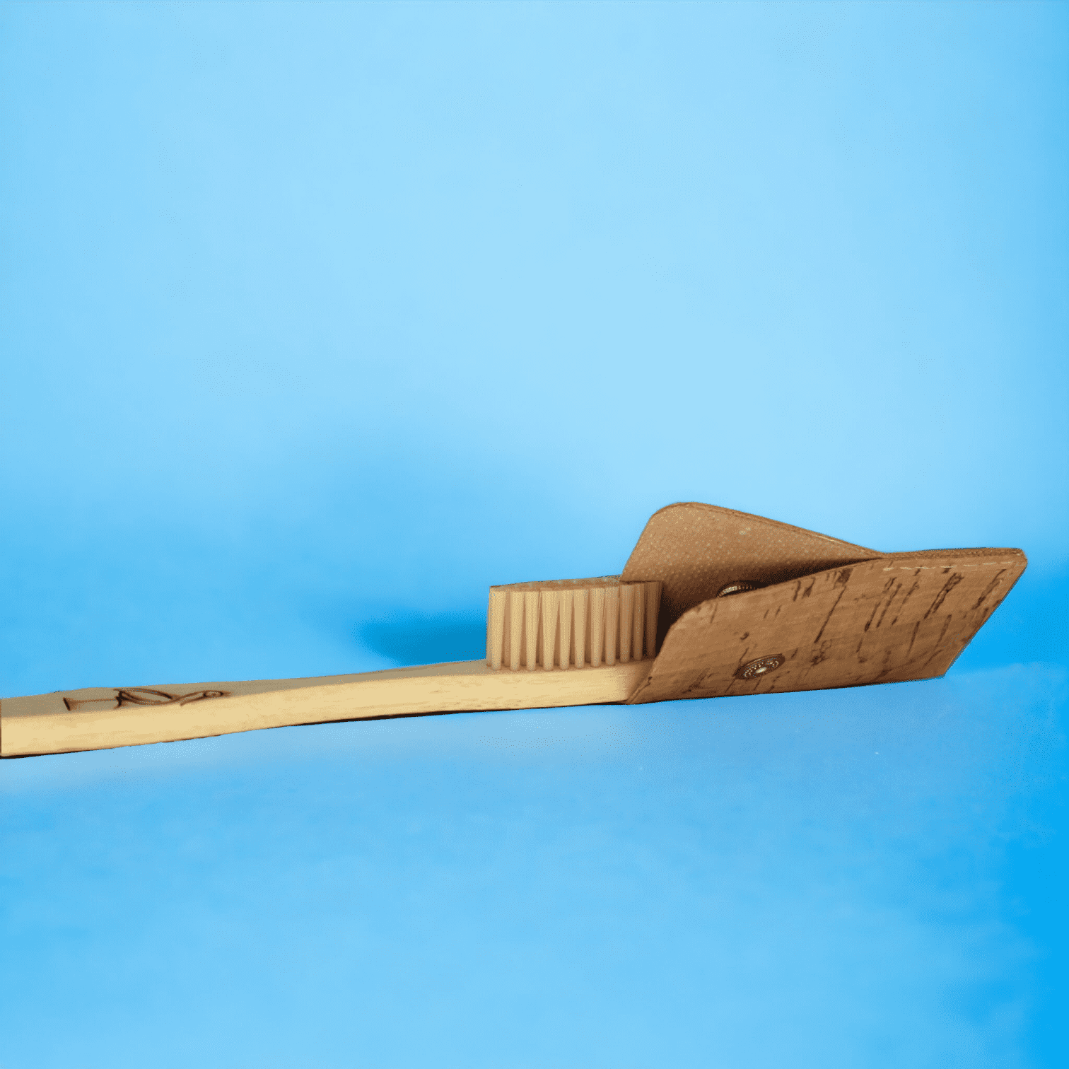 Zahnbürsten-Schutzhülle wie sie über eine Holzzahnbürste gezogen wird vor blauem Hintergrund