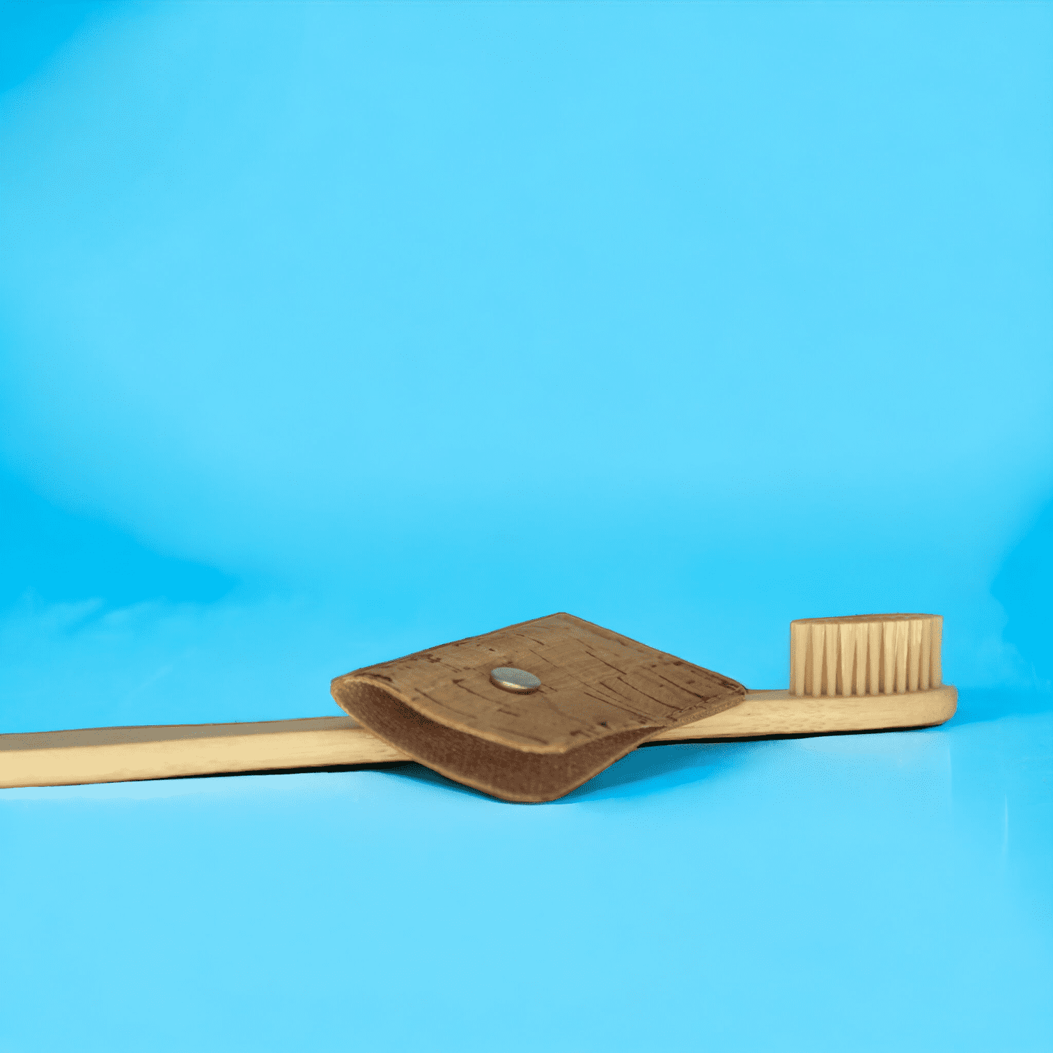 Zahnbürsten-Schutzhülle liegend auf einer Holzzahnbürste vor blauem Hintergrund