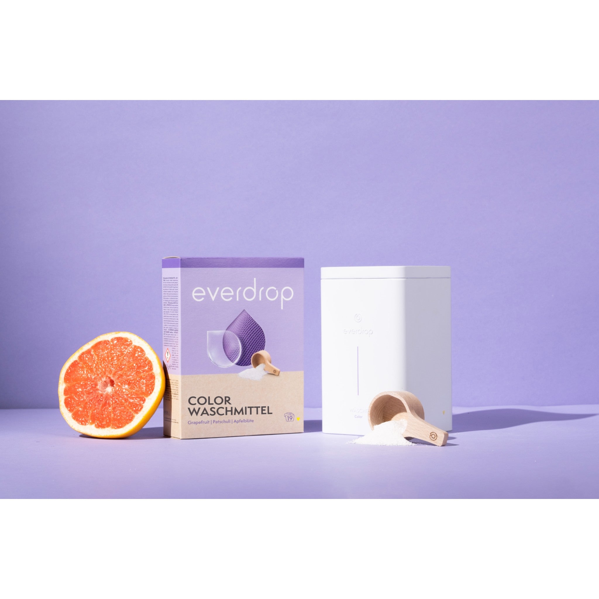 everdrop colorwaschmittel mit einer halben grapefruit und einem aufbewahrungsbehälter vor lila hintergrund